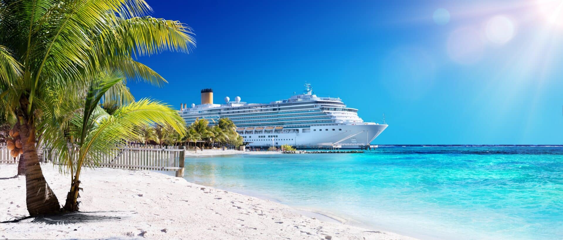 Kreuzfahrtschiff an karibischem Strand mit Palmen