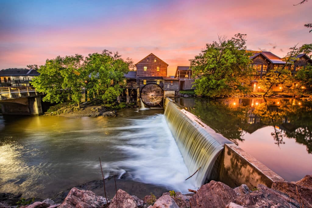 Eine historische Wassermühle (Old Mill) am Wasserfall in Pigeon Forge, Tennessee, bei Sonnenuntergang.