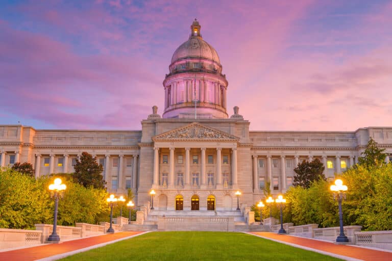 Das Kentucky State Capitol Gebäude bei Sonnenuntergang, mit erleuchteten Laternen entlang des Weges und einem rosa-violetten Himmel im Hintergrund.