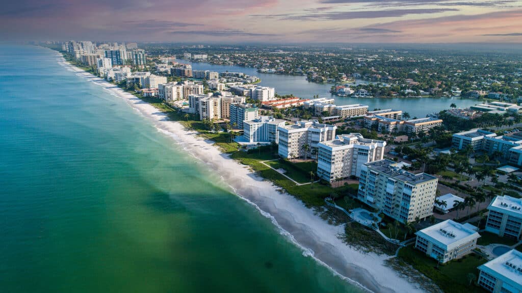 Eine Luftaufnahme der Küstenlinie von Naples, Florida. Strand und Wohnkomplexe sind neben dem türkisfarbenen Meer zu sehen.