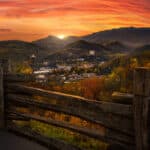 Landschaftsaufnahme der Stadt Gatlinburg, Tennessee, und der umliegenden Berge bei Sonnenuntergang. Im Vordergrund ist ein Holzzaun zu sehen.