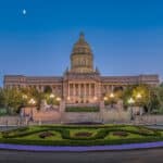 Das Kentucky State Capitol in Frankfort bei Dämmerung, beleuchtete Laternen und ein gepflegter Vorplatz sind im Vordergrund. Der Mond ist am Himmel sichtbar.