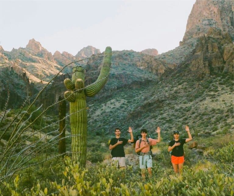 Drei Wanderer neben einem riesigen Saguaro-Kaktus ahmen mit ihren Armen dessen Form nach